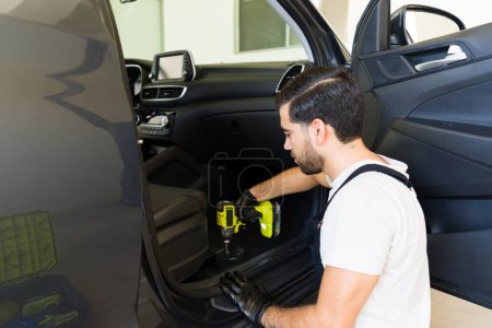 Photo for Hispanic male worker removing seats of car with cordless impact gun to clean interiors at auto detailing service station - Royalty Free Image