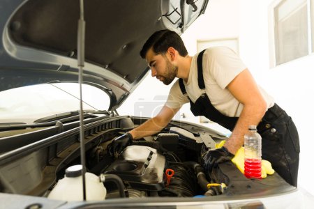 Photo for Handsome young man polishing engine cover of a car while working at the auto detail service - Royalty Free Image