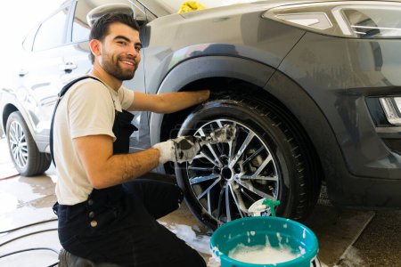Téléchargez les photos : Heureux jeune mexicain employé masculin laver un véhicule au lavage de voiture - en image libre de droit