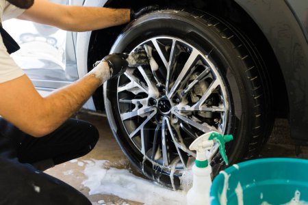 Foto de Primer plano de un hombre que trabaja en el lavado del neumático del coche con jabón y un cepillo en un lavado de coches - Imagen libre de derechos