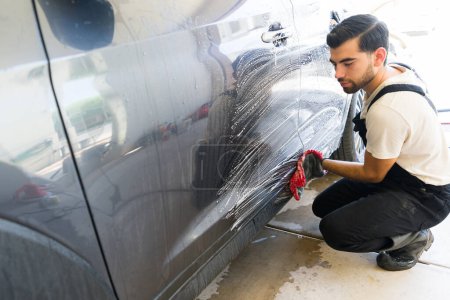 Photo for Latin man working at auto detail service washing a customer vehicle with foam - Royalty Free Image