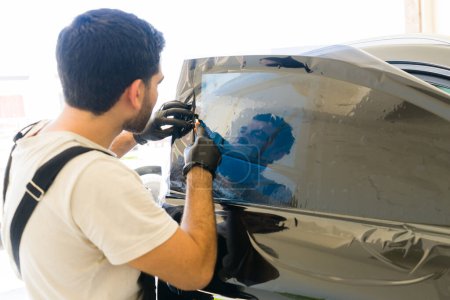 Photo for Rear view of a male employee installing tinting film on car window at auto detail service - Royalty Free Image