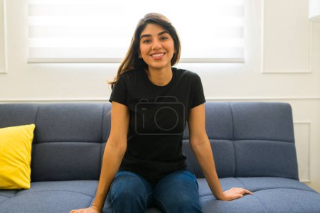 Foto de Hermosa mujer joven buscando feliz relajarse en el sofá con una camiseta mockup negro casual - Imagen libre de derechos
