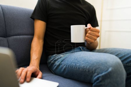 Téléchargez les photos : Gros plan d'un jeune homme buvant du café à l'aide d'une tasse blanche de 11 oz et d'un t-shirt noir maquillé - en image libre de droit