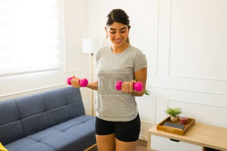 Téléchargez les photos : Active fit jeune femme faisant de l'exercice à la maison soulevant haltère poids portant un t-shirt gris maquette - en image libre de droit