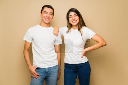 Téléchargez les photos : Joyeux couple attrayant souriant tout en portant des t-shirts blancs assortis sur fond de studio - en image libre de droit
