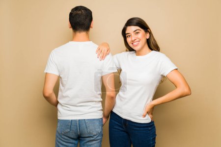 Téléchargez les photos : Homme et femme attirants montrant l'avant et l'arrière d'un t-shirt blanc assorti sur fond de studio - en image libre de droit