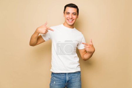 Téléchargez les photos : Beau caucasien jeune homme pointant vers son blanc maquette t-shirt avec copie espace conception - en image libre de droit