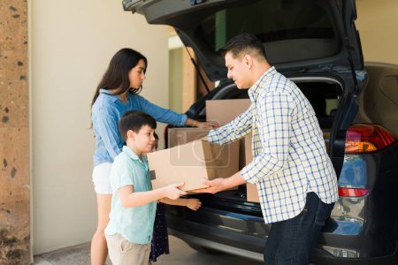 Téléchargez les photos : Enfant aidant ses parents à transporter des boîtes en carton de la voiture tout en déménageant dans une nouvelle maison ou un appartement de location - en image libre de droit