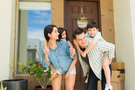 Photo for Excited family with children piggybacking having fun moving into a new home together playing in the house entryway - Royalty Free Image