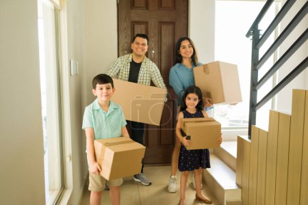 Photo for Mom and dad with two children carrying boxes arriving to their new home after buying or renting a house and moving in - Royalty Free Image