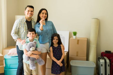 Téléchargez les photos : Portrait d'une famille heureuse avec deux enfants souriant et déballer des boîtes dans leur nouvelle maison ou appartement tout en déménageant - en image libre de droit