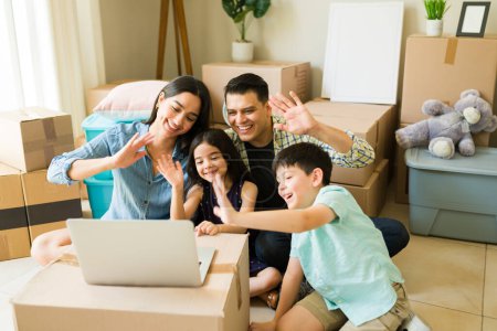 Foto de Alegre mamá y papá con los niños saludando a su familia durante una videollamada en línea en el portátil después de mudarse a una nueva casa - Imagen libre de derechos