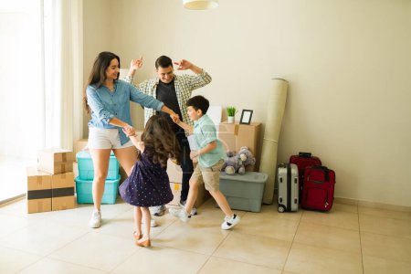 Foto de Mamá y papá latinos se divierten bailando con sus hijos mientras se mudan a una nueva casa y desempacan cajas - Imagen libre de derechos