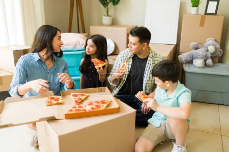 Photo for Beautiful happy family relaxing after unpacking a lot of boxes and moving into a new house and eating pizza for dinner - Royalty Free Image