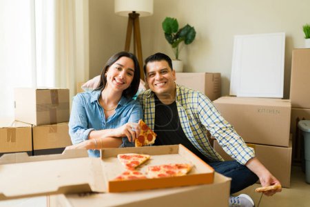 Photo for Portrait of a happy attractive couple hugging and eating pizza together celebrating getting a mortgage and moving to a new house - Royalty Free Image