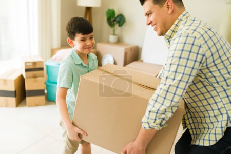 Photo for Happy father and his kid smiling while unpacking cardboard boxes and moving into a new house or apartment - Royalty Free Image