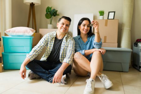 Téléchargez les photos : Couple mexicain jeunes mariés déballer les meubles et les boîtes après avoir obtenu un crédit pour acheter une nouvelle maison ensemble regardant heureux - en image libre de droit