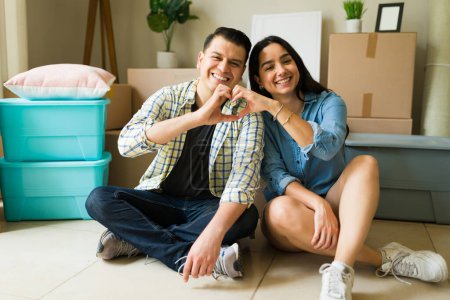Téléchargez les photos : Un mari et une femme aimants faisant un geste de cœur avec leurs mains tout en emménageant dans une nouvelle maison et se sentant amoureux - en image libre de droit