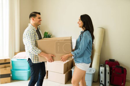 Téléchargez les photos : Couple joyeux portant des boîtes en carton ensemble et déballer dans leur nouvelle maison ou appartement en tant que jeunes mariés - en image libre de droit