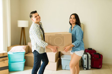 Téléchargez les photos : Couple latin mexicain portant des boîtes en carton et des meubles à leur nouvelle maison tout en souriant faire contact avec les yeux - en image libre de droit
