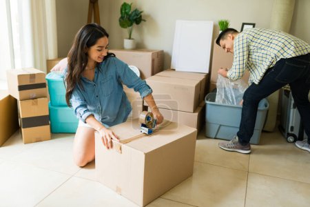 Photo for Mexican couple of husband and wife packing boxes and moving out of the apartment after buying a new house together - Royalty Free Image