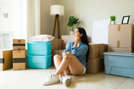 Photo for Beautiful hispanic woman dreaming about her new house after moving in and unpacking boxes at the apartment - Royalty Free Image