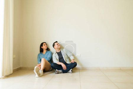 Téléchargez les photos : Couple hispanique jeunes mariés se détendre et rêver de leur nouvelle maison et acheter des meubles après avoir emménagé ensemble - en image libre de droit