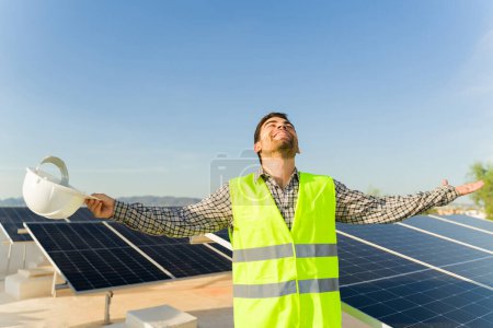 Foto de Ingeniero hombre excitado con un chaleco de seguridad y casco celebrando el acabado de la instalación de paneles solares y células fotovoltaicas - Imagen libre de derechos