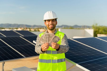 Foto de Alegre instalador ingeniero sonriendo ganar un montón de dinero mirando emocionado acerca de trabajar en la instalación de energía solar - Imagen libre de derechos