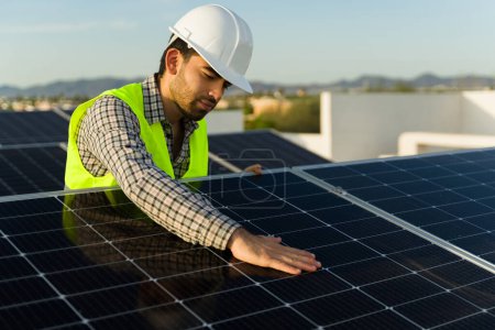 Photo for Hispanic handsome man with a helmet working as a solar panel installer and engineer checking the photovoltaic cells - Royalty Free Image