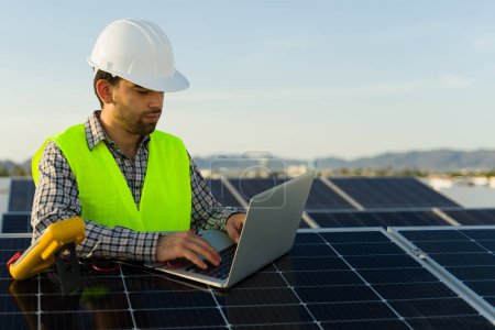 Photo for Attractive engineer typing on the laptop using the voltage multimeter after working on the solar panel installation - Royalty Free Image
