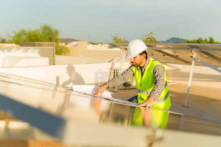 Foto de Ingeniero masculino mirando los planos de instalación de los paneles solares y las células fotovoltaicas en la casa residencial - Imagen libre de derechos