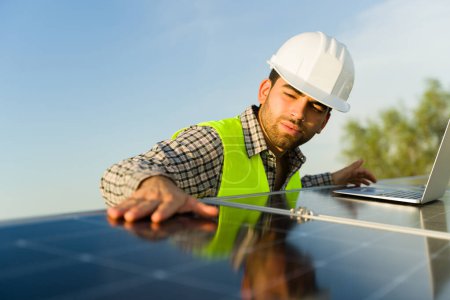 Foto de Ingeniero atractivo comprobando los paneles solares y las células fotovoltaicas en el techo de la casa con un chaleco de seguridad y casco - Imagen libre de derechos