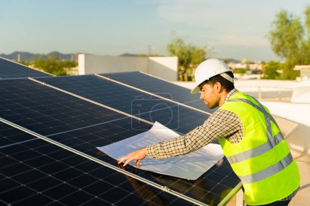 Téléchargez les photos : Ingénieur installateur regardant les plans d'installation des panneaux solaires du toit résidentiel tout en travaillant avec de l'énergie propre - en image libre de droit