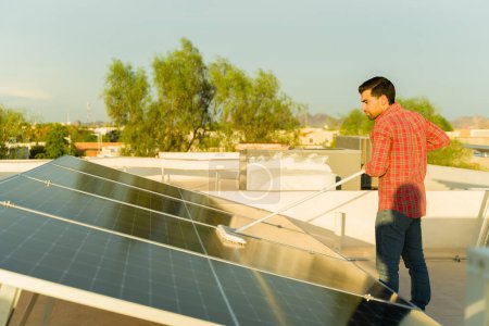 Foto de Joven latino limpiando los paneles solares y las células fotovoltaicas de su hogar residencial para generar energía sostenible - Imagen libre de derechos