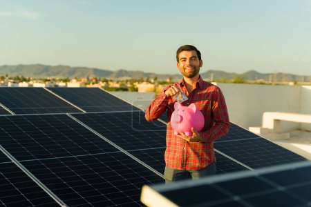 Porträt eines glücklichen jungen Mannes, der Geld spart, indem er grüne nachhaltige Energie und Sonnenkollektoren oder Photovoltaikzellen verwendet