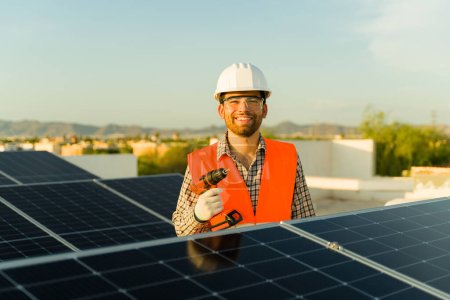 Photo for Cheerful engineer worker smiling using a drill during solar panels installations at a residential home rooftop - Royalty Free Image
