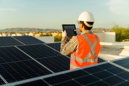 Photo for Rear view of a male engineer worker with an orange vest and safety helmet taking a picture after a solar panel installation - Royalty Free Image