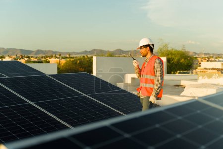 Téléchargez les photos : Homme ingénieur installateur parler à la radio ou talkie walkie sur les panneaux solaires de travail sur la maison de toit résidentiel - en image libre de droit