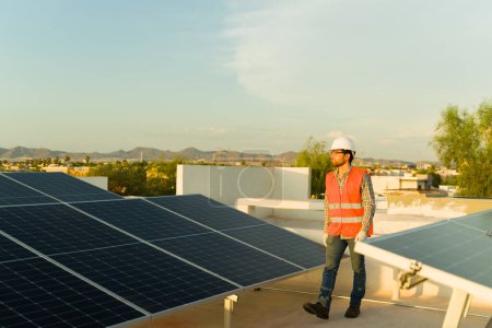 Photo for Latin engineer with an orange vest and safety helmet working as a solar panel and photovoltaic cell installer at a residential home rooftop - Royalty Free Image