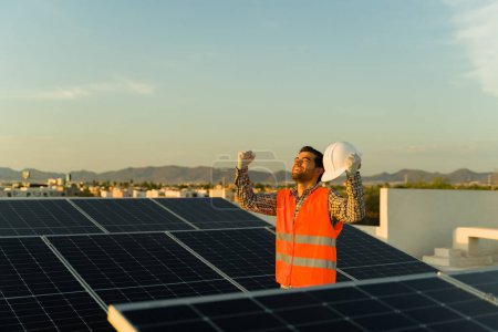 Téléchargez les photos : Travailleur ingénieur excité souriant et célébrant la finition d'un panneau solaire et d'une installation de cellules photovoltaïques dans une résidence - en image libre de droit