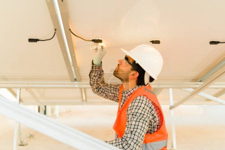 Photo for Engineer man with a vest and helmet working on installing the electrical connection of the solar panels - Royalty Free Image