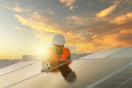 Foto de Ingeniero atractivo con un casco de seguridad que trabaja como instalador de paneles solares usando energía verde limpia contra un hermoso cielo al atardecer - Imagen libre de derechos