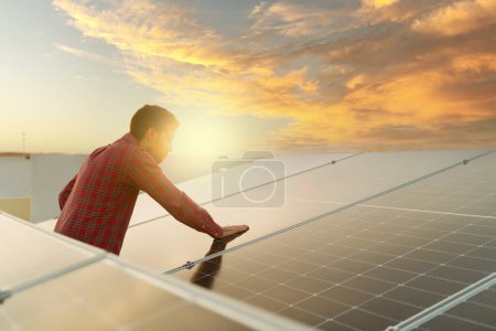 Téléchargez les photos : Jeune homme attrayant se sentant heureux d'utiliser de l'énergie verte propre à la maison et d'installer des panneaux solaires ou des cellules photovoltaïques - en image libre de droit