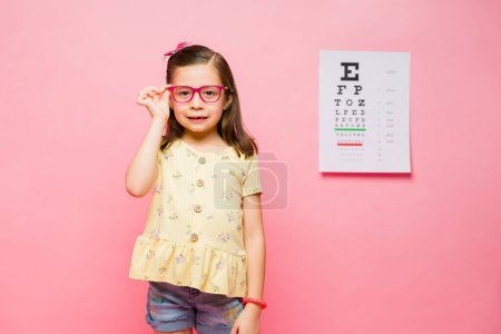 Téléchargez les photos : Heureux petit caucasien à l'optométriste obtenir des lunettes de prescription en raison de l'astigmatisme et sourire - en image libre de droit