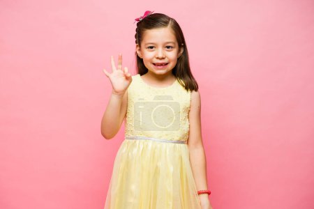 Photo for Happy beautiful little girl in a pink studio background making a perfect excellent gesture while smiling feeling happy - Royalty Free Image
