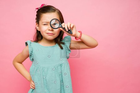 Téléchargez les photos : Petit enfant élémentaire utilisant une loupe jouant un jeu de détective espion à côté de copier l'espace fond rose - en image libre de droit