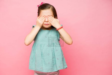 Foto de Adorable niña mirando asustada y cubriéndose los ojos después de mirar algo aterrador al lado del espacio de copia rosa - Imagen libre de derechos