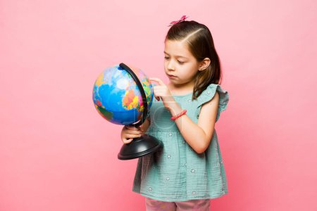 Foto de Adorable niño de edad elemental que busca un país mientras aprende geografía educación usando un globo en la escuela - Imagen libre de derechos